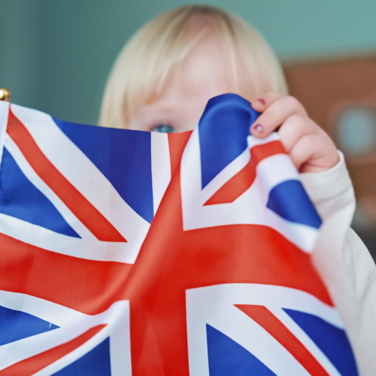 English flag in child's hands. Little girl with blond hair closes her face with the British flag. Cute child holds the flag of Great Britain. Close-up.