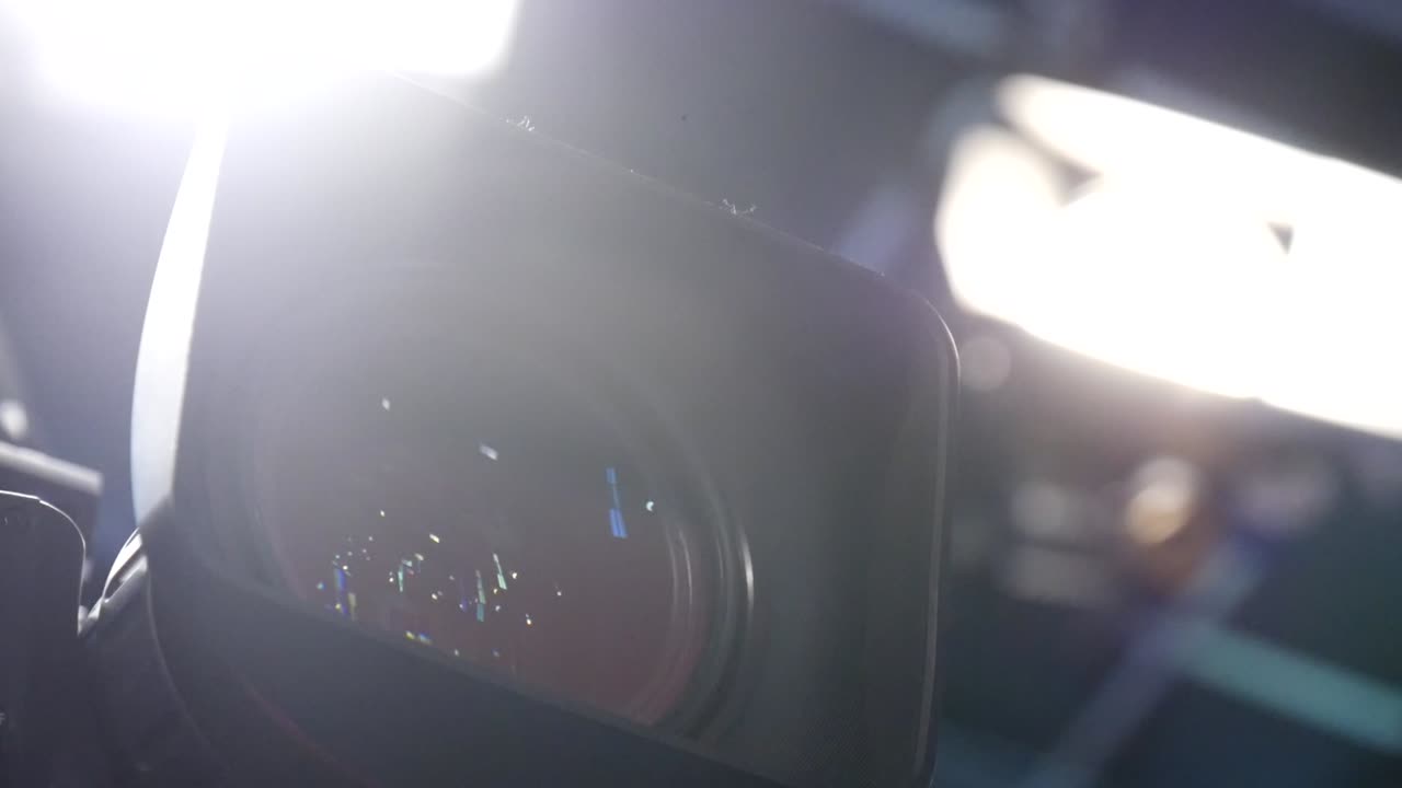 primer plano de la lente de una cámara de vídeo con luces de producción brillantes en el set