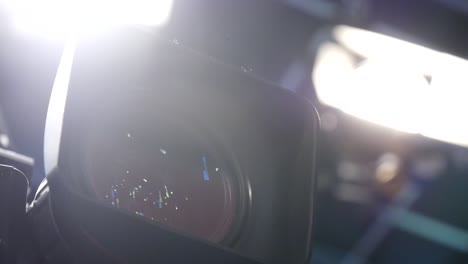 close-up of a video camera lens with bright production lights on set