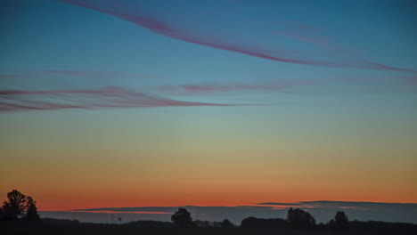 wispy clouds cross the sky above the wooded horizon at dawn - wide angle sunrise time lapse