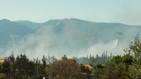 Wide-view-of-firefighter-helicopter-spraying-water-on-forest-fire-at-Parnitha-mountain,-Greece-,-slow-motion-120fps