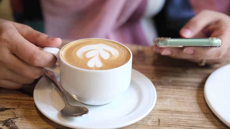 Donna che si gusta un latte e usa il telefono in un bar