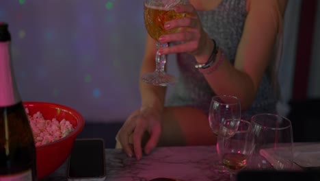 beautiful blonde caucasian white girl women in front of led light wall in a dark night club scene neck down shot as she drinks from champagne wine glass and popcorn as lights flash at night club