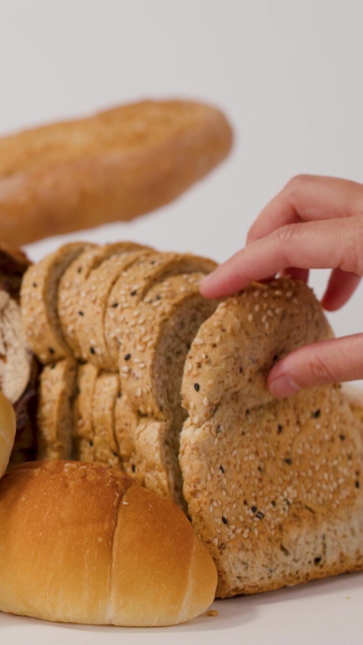 Close-up shot of hands selecting sliced seeded bread from a variety of fresh pastries.