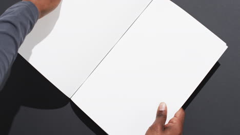 Video-of-hand-of-african-american-man-holding-book-with-blank-pages,-copy-space-on-black-background