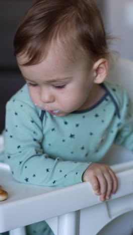 nourishing baby boy sitting in the chair. mom is shoving the full spoon to a boy but he is distracted by something else and turned away. vertical video
