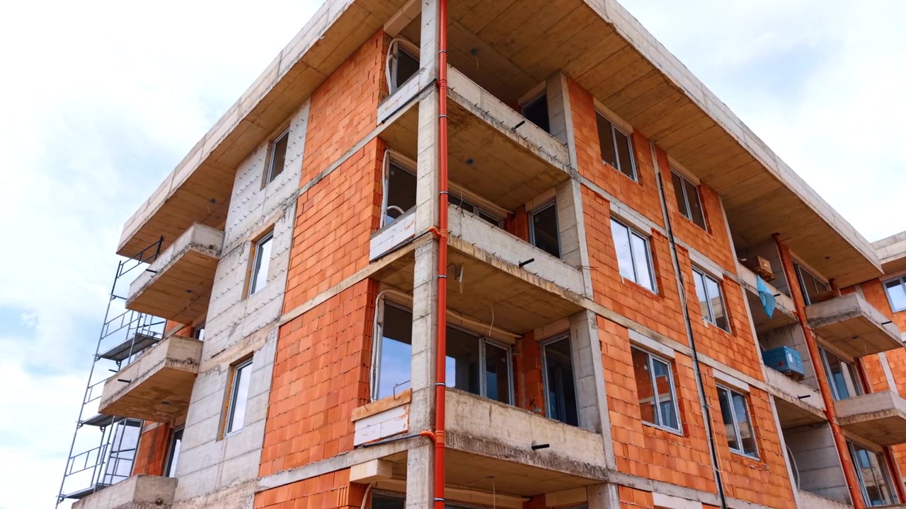 Vista de baixo ângulo da construção de um edifício residencial de vários andares. Perspectiva de canto de um edifício de apartamentos inacabado com paredes de tijolo e varandas de concreto.