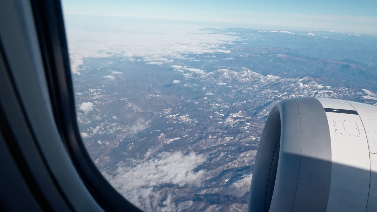 Luftaufnahme aus dem Flugzeugfenster zeigt schneebedeckte Berge und Wolken.