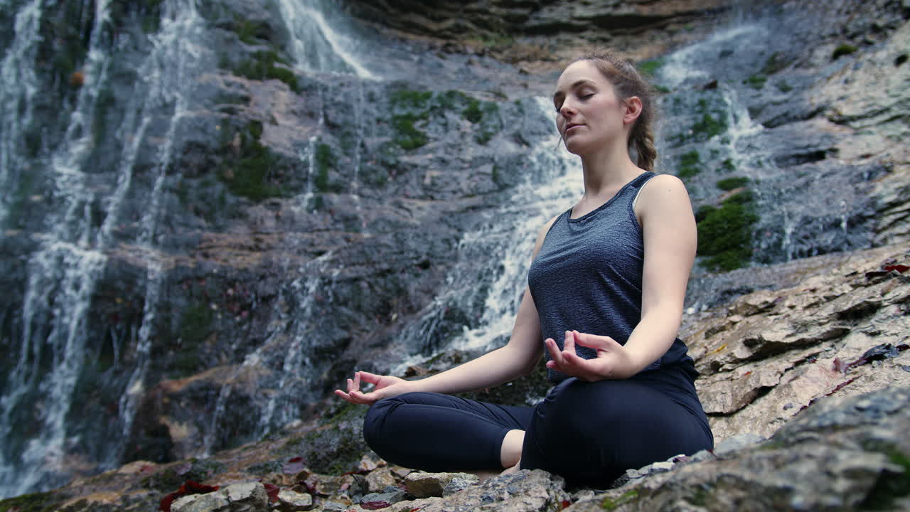 mujer meditando junto a la cascada y conectándose con la naturaleza, toma de ángulo bajo