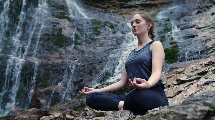 Mujer meditando junto a la cascada y conectando con la naturaleza, toma en ángulo bajo