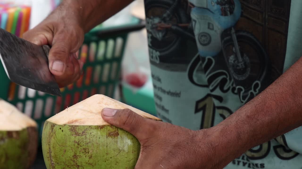 A vendor expertly slices a coconut using a machete, showcasing skillful hand movements.