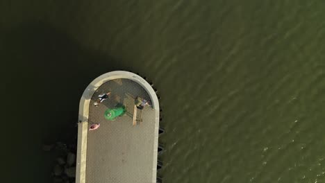 people on pier with small green lighthouse and breakwater