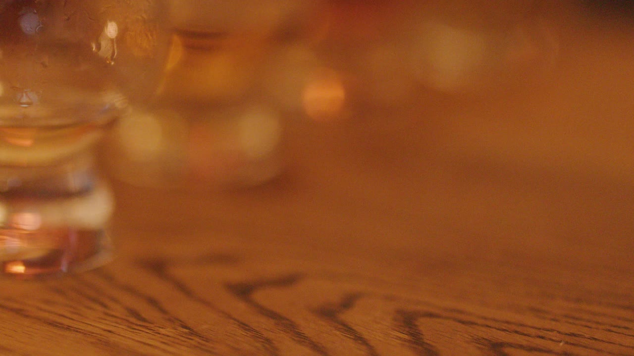 Slow pan of whiskey glasses with amber liquid on rustic wood table under warm lighting