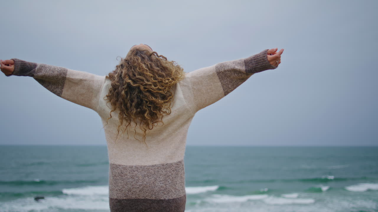 mujer de vacaciones sintiendo libertad relajándose en la costa nublada del océano vista trasera de primer plano.