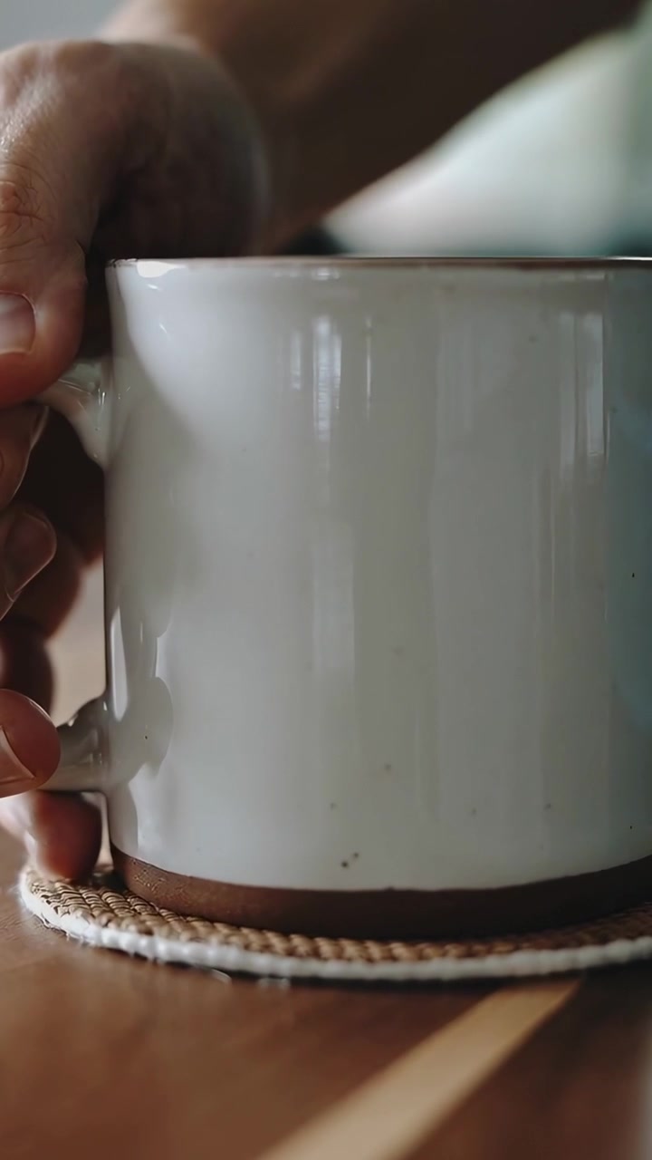 Video verticale: Una mano che si abbassa, posizionando una tazza su un sottobicchiere su un tavolo per proteggerlo, con una manica chiara.