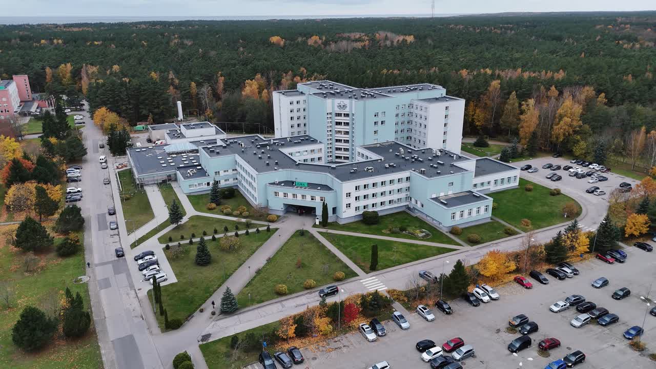 Modern hospital complex surrounded by trees and parking lot in autumn aerial view