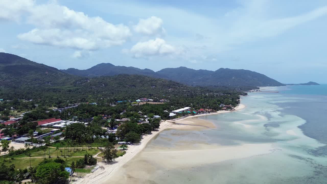 Aerial footage of Thong Sala Beach with a wide sandy shoreline, turquoise sea and lush tropical scenery on Koh Phangan island, Thailand
