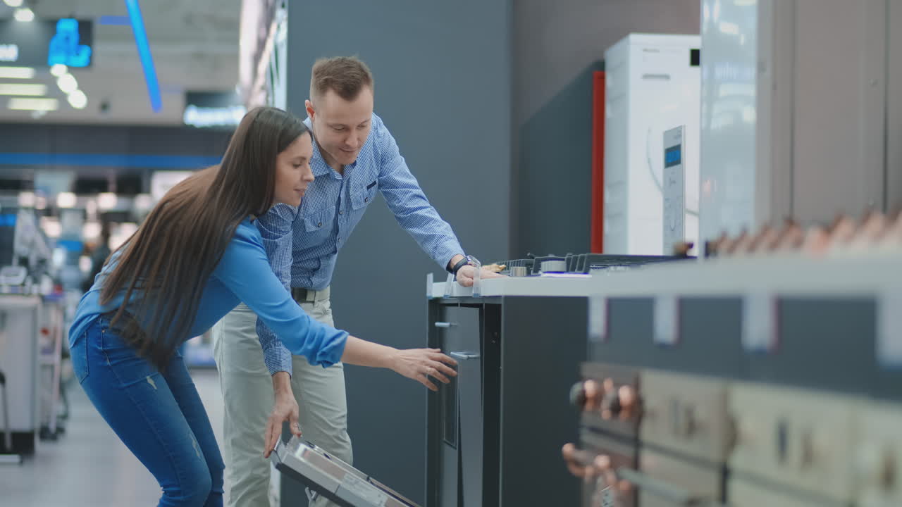el hombre y la mujer para abrir la puerta de los aparatos de lavavajillas en la tienda y comparar con otros modelos para comprar la nueva casa