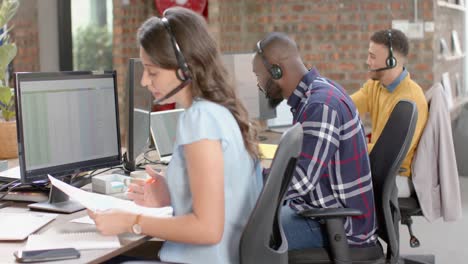 caucasian businesswoman holding a document talking on phone headset at office