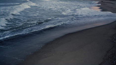 dark sea waves splashing sandy beach outside. blue ocean water crashing shore.