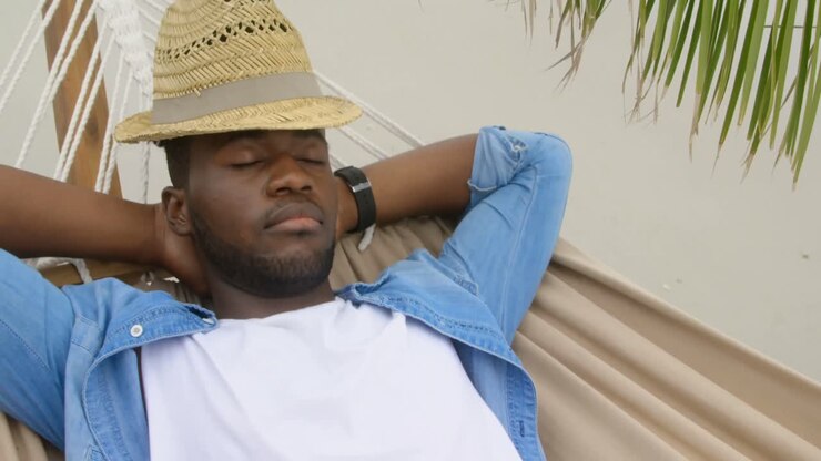 Uomo afroamericano ripreso dall'alto che dorme su un'amaca in spiaggia 4K