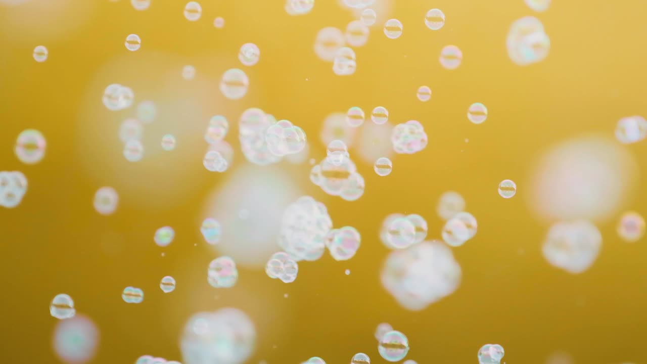 색 비누 거품이 노란색 배경에서 느린 동작으로 날아다닙니다.