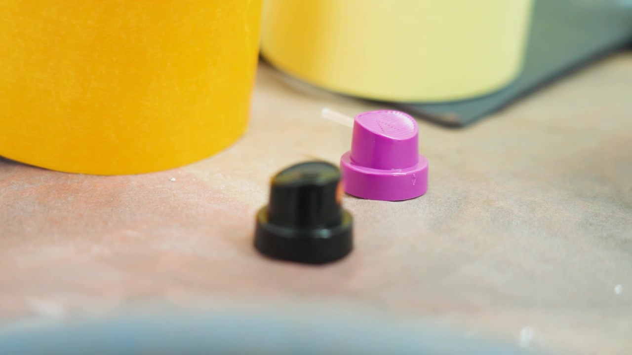 Tappi colorati per bombolette spray e accessori per vernici automobilistiche su un tavolo da officina in un ambiente di carrozzeria professionale per la riverniciatura di veicoli e processi di riparazione industriale, UHD