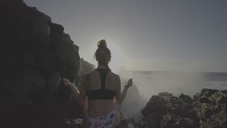 woman meditating on a rocky beach at sunrise