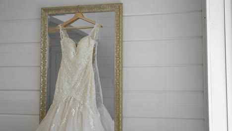 elegant commercial graded film of a white wedding gown hanging in a gold outlined mirror in a clean white room at the le belvédère in wakefield, quebec, canada