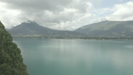 Aufschlussreiche-Drohnenaufnahme-Der-Berge-Hinter-Dem-See-Von-Annecy-In-Frankreich,-Europa-An-Einem-Bewölkten-Tag-Mit-Blauem-Wasserstamm