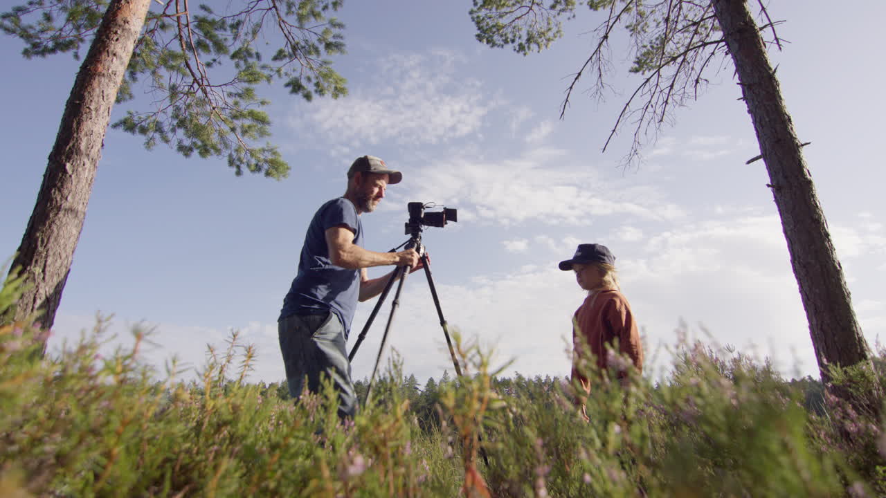 Videographer use camera on tripod in woods to record video of young boy, profile