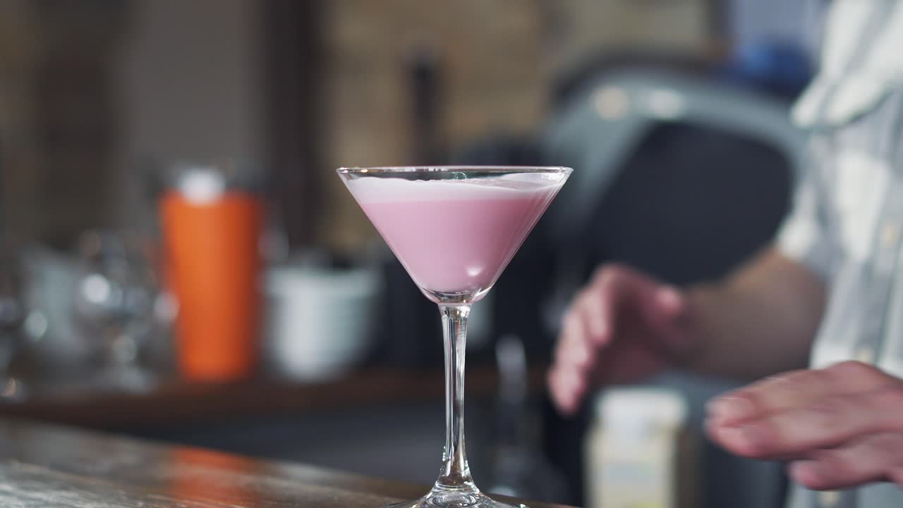 Barman placing delicious pink cocktail in a glass on the bar counter for client. Glass of tasty cocktail for party
