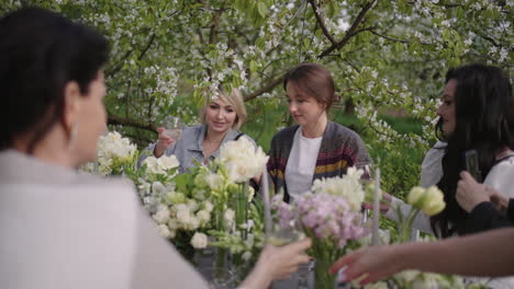 feast-in-garden-people-are-sitting-at-table-with-flowers-decoration-drinking-wine-and-clinking-glasses