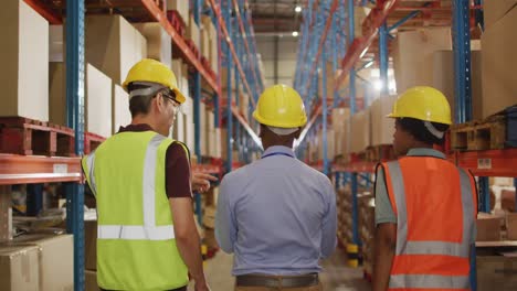 diverse male and female workers wearing safety suits and talking in warehouse