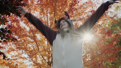 a cheerful child in a deer costume dances near a beautiful autumn tree