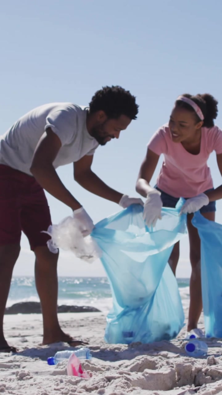Animazione del simbolo del riciclo su una coppia afroamericana che pulisce in spiaggia