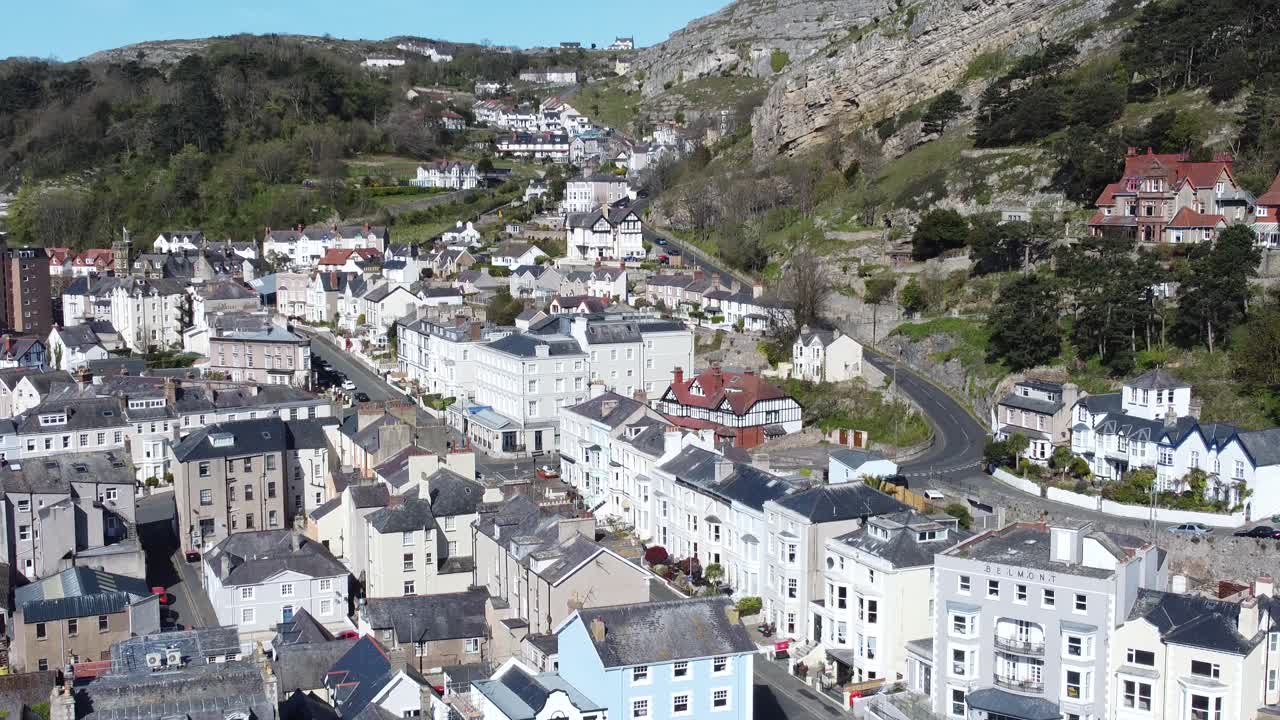 Vista aerea con lenta inclinazione verso l'alto degli hotel colorati della città balneare di Llandudno, con il monte Great Orme sullo sfondo.