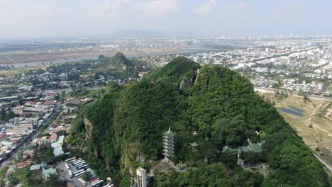 drone vista aérea en vietnam volando sobre la ciudad de da nang montañas de mármol llenas de árboles con templos budistas rodeados de tierra plana en un día soleado