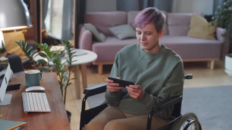 woman in wheelchair using mobile phone at home office