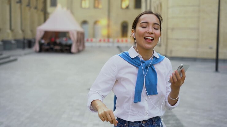 Donna allegra che balla e ascolta musica camminando verso la fotocamera all'aperto 1