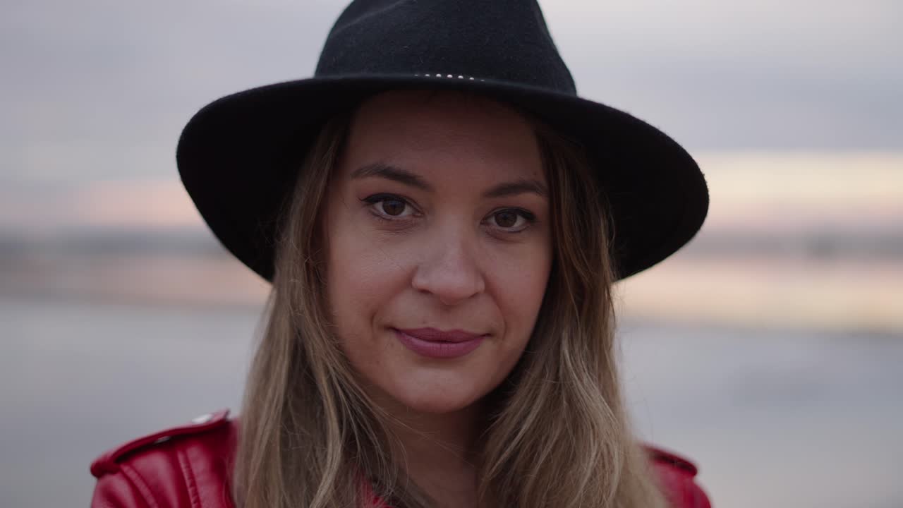 Woman in a Red Jacket and Black Hat at the Beach at Sunset