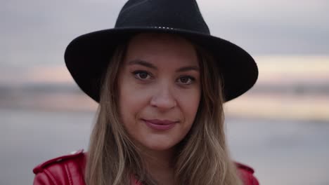 woman in a red jacket and black hat at the beach at sunset
