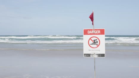 close up danger sign and red flag on empty australian beach.