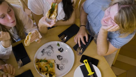 Top-View-Of-A-Group-Of-Four-Happy-Friends-Sharing-Pizza-And-Talking-At-Restaurant