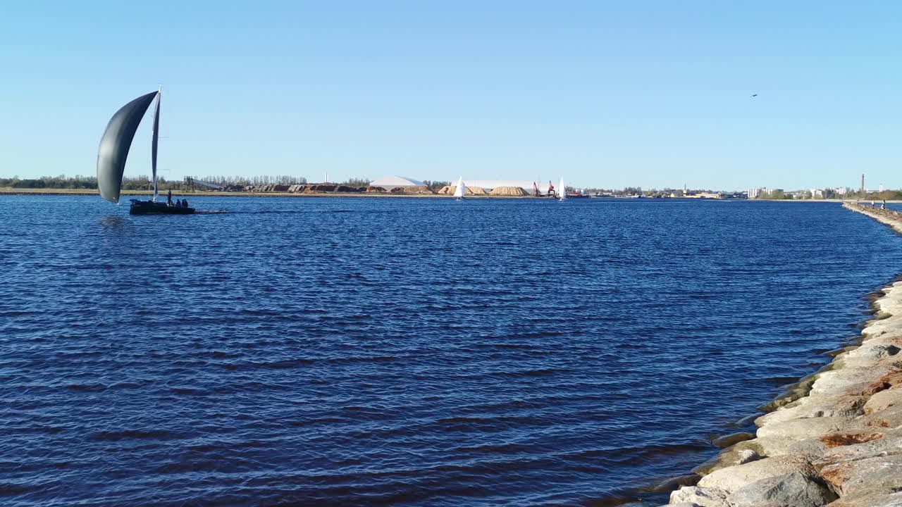Sailboat with black sails passing on Calm Waters Alongside Rocky Shoreline
