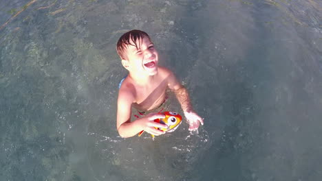 high view of a toddler jumping and splashing a fish toy in the sea waters