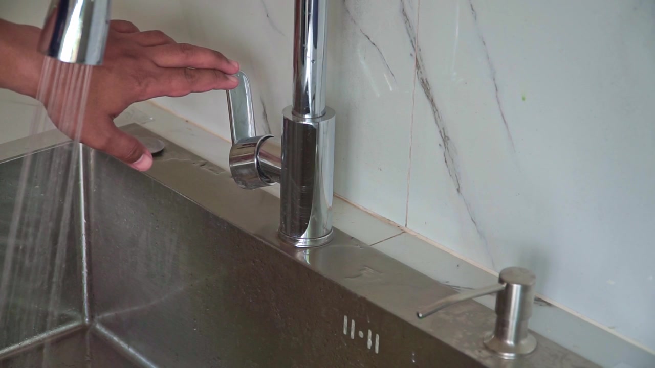 Mano che apre il rubinetto dell'acqua in un moderno lavello da cucina. Concetto di igiene e utilità domestica.