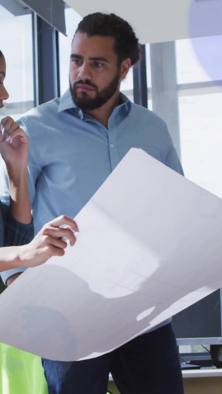 Vertical video: Two colleagues unfolding and reviewing blueprint at table, pointing to adjust plan