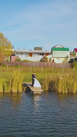 happy young couple stands on small calm river pier near cottage village houses on sunny day aerial view