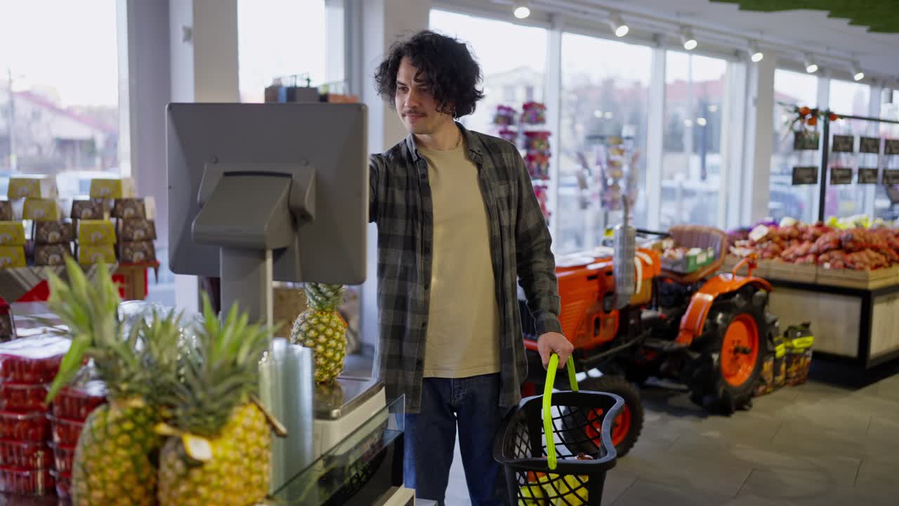 un tizio con i capelli ricci in una camicia pesa ananas usando la bilancia in un supermercato mentre fa shopping in un negozio di alimentari